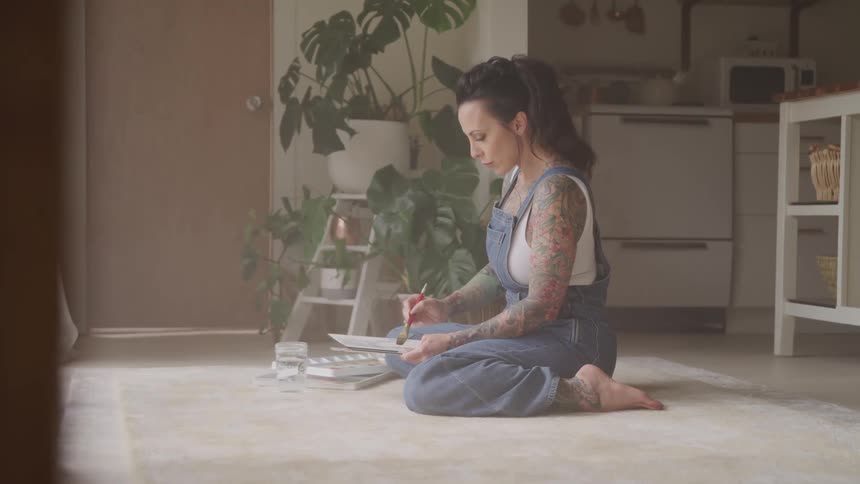 A woman kneels on the flooring painting in her apartment