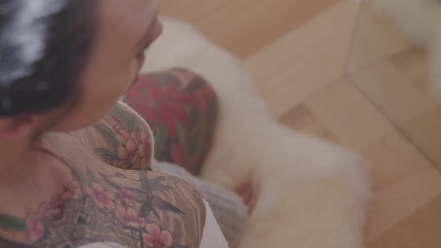 Heavily tattooed woman wearing underwear sits on the rug in the living room