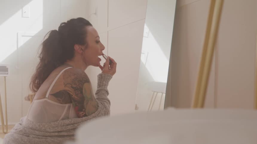 A woman looks in the mirror to put lipstick on
