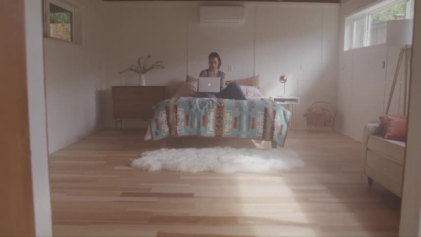 A white woman uses a laptop computer while sitting on a bed