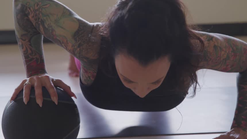 A tattooed woman doing push ups with an exercise ball