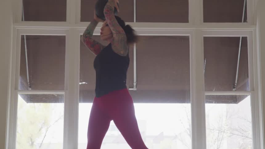 Woman working out with a medicine ball in front of large window indoors