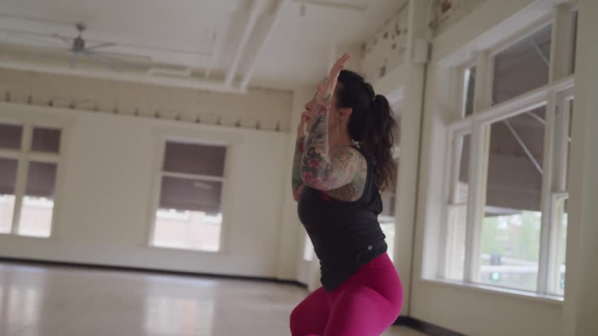 A woman with tattoos on her arms squatting and stretching