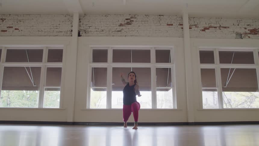 Woman performs yoga on shiny reflective floor near wide windows