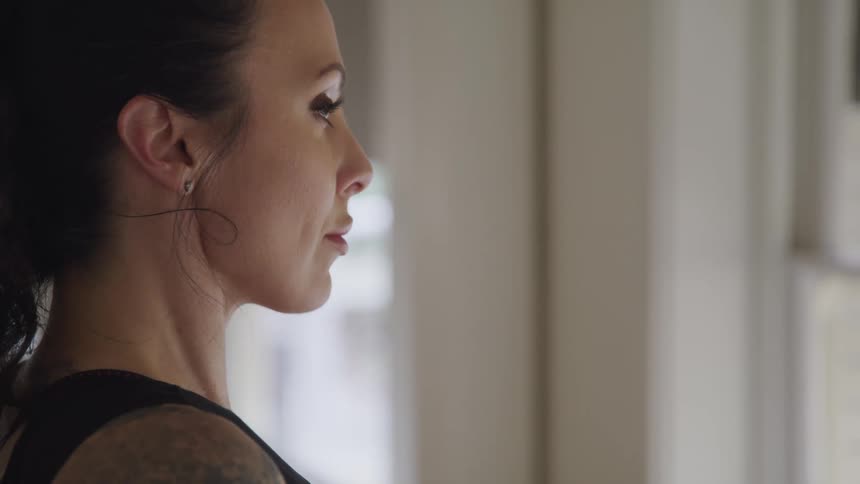 Tattooed woman stands and looks ahead in the living room