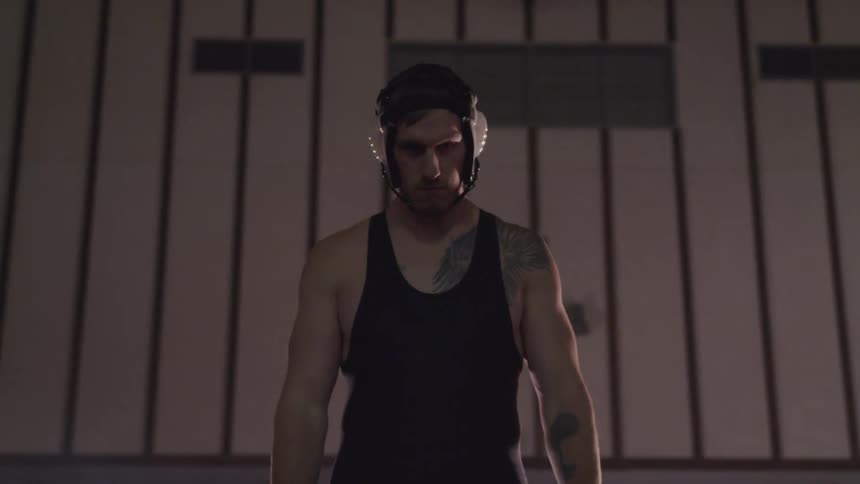 Tattooed young man wearing wrestling equipment waiting in gym