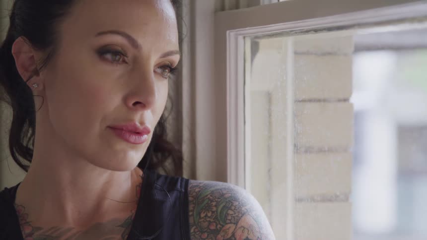 Heavily tattooed woman sitting on the window ledge looks out the window