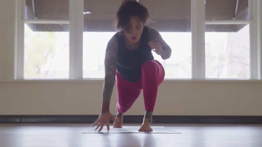 A white woman in yoga attire stretches on a mat in a room