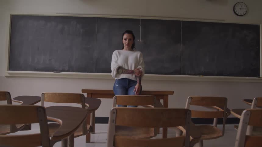 A woman leans against the desk in the classroom