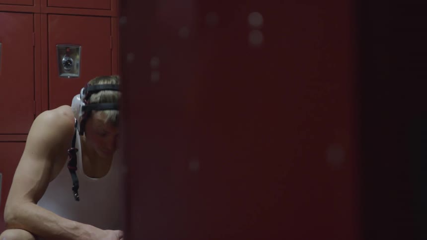 A man in a white leotard sitting in a locker room