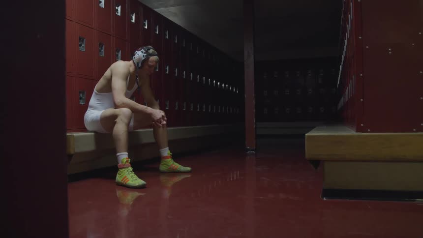 A wrestler sits by himself in a locker room