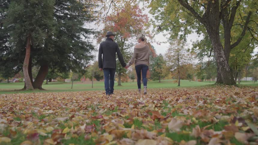 A man and woman hold hands walking in the park
