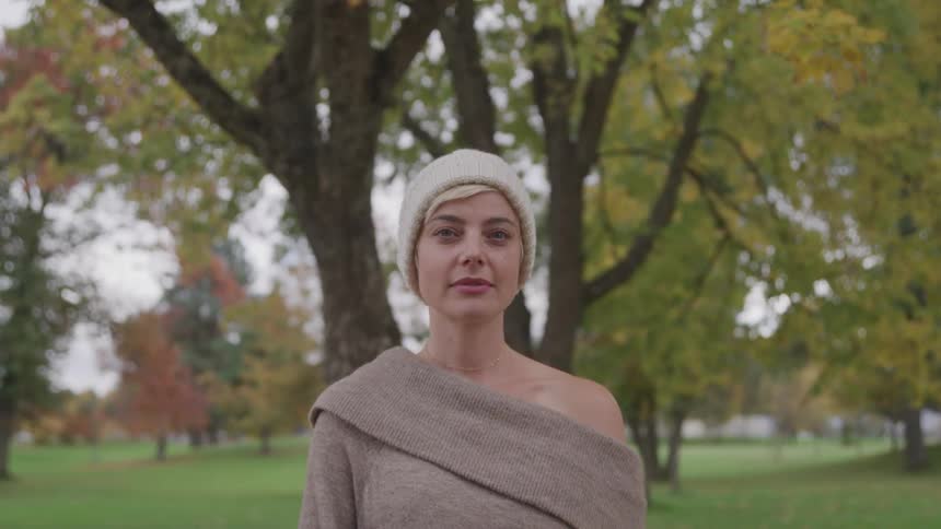 Female in knit beanie standing front of large tree at a park during fall colors