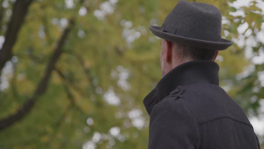 Man wearing a hat and coat standing looking at fall colors on tree
