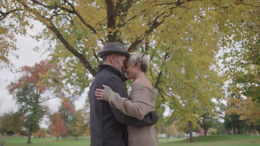 An elderly husband and wife embrace and slow dance in a park