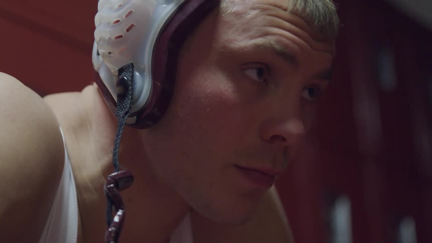 Close up of young mans face sitting in locker room wearing wrestling equipment