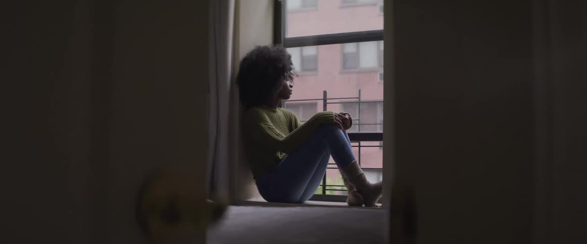 A woman sits close to a window and looks outside