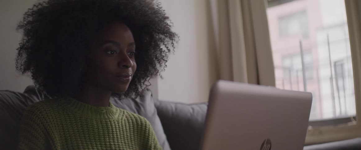 Afro curly haired woman sitting on the sofa uses a laptop in the living room