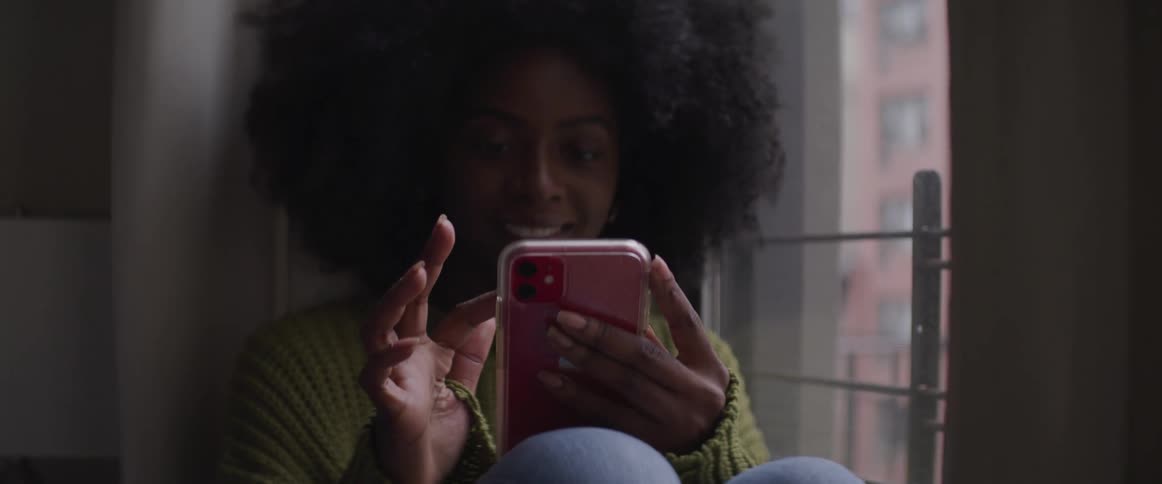 A woman sits next to a window and scrolls through her cell phone