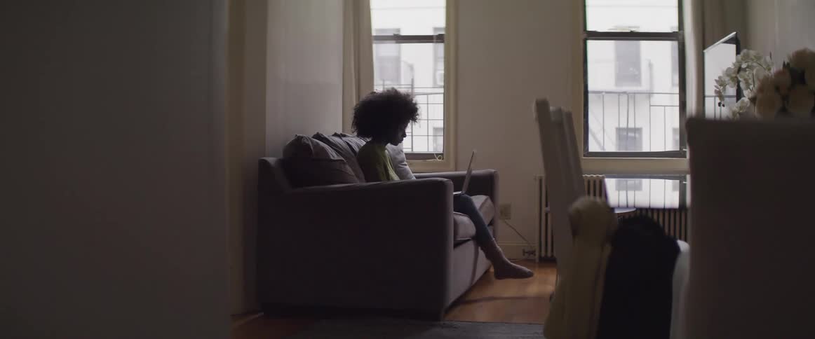 Afro curly haired woman sitting on the sofa uses a laptop in the living room at home