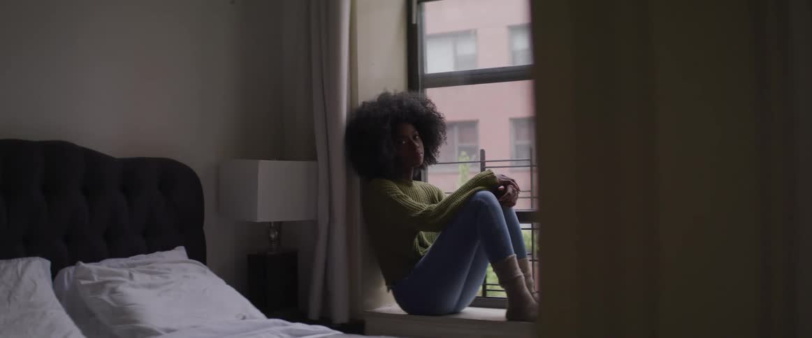 Black woman sits on an interior window ledge in a bedroom