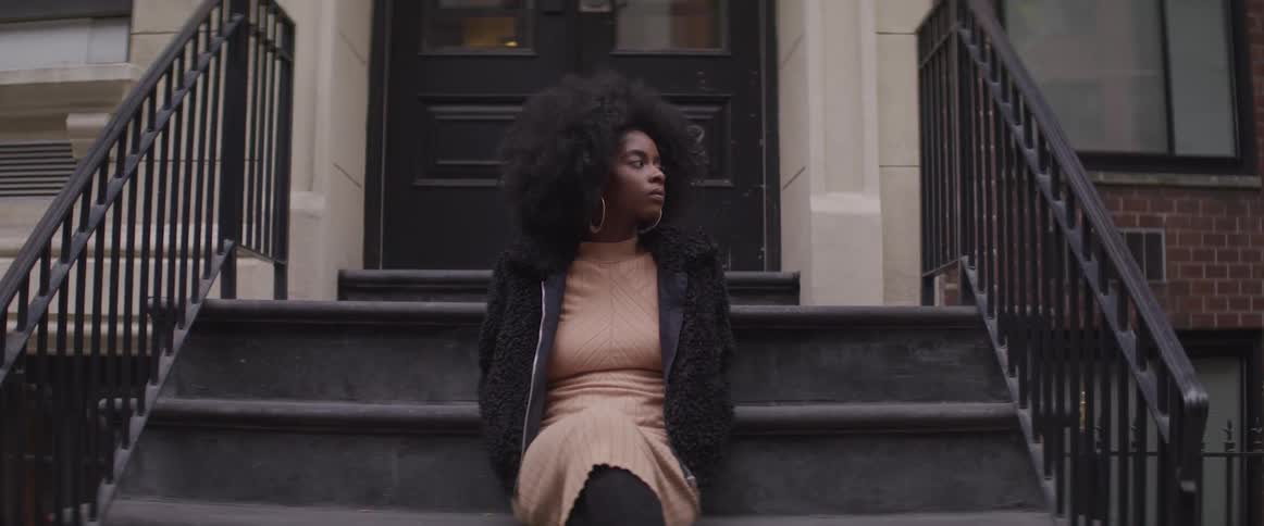 Young black woman sitting on front steps looking off to the side