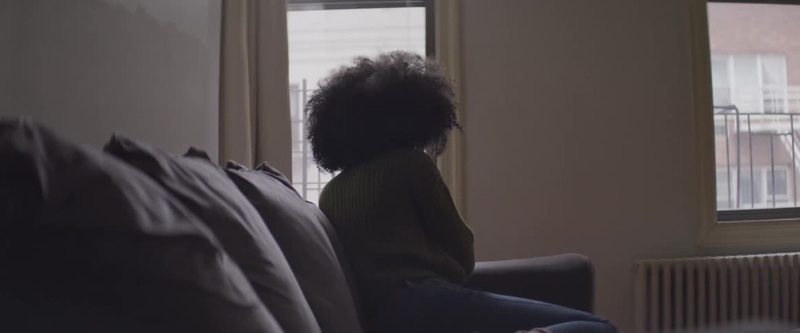 A woman sits on a couch and stares out the window