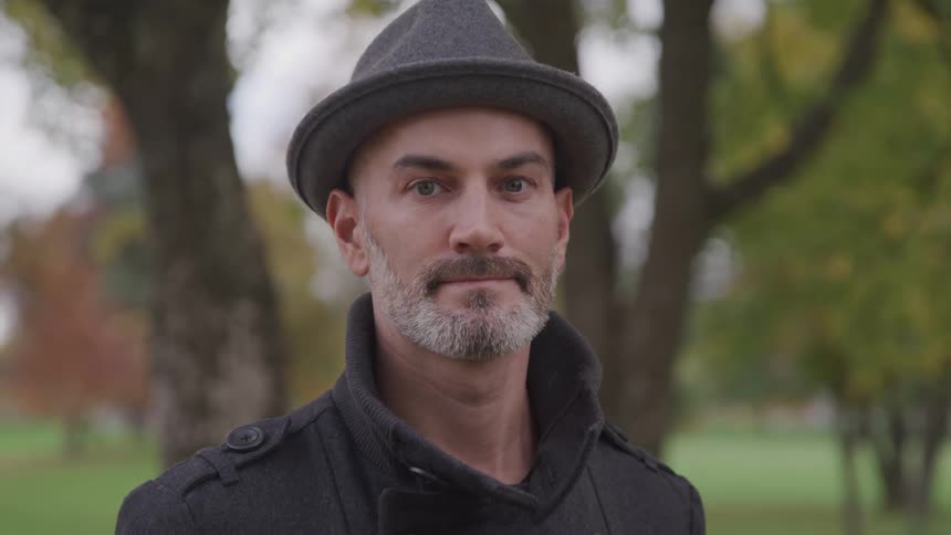 A slowly turning his head to look into the camera while standing outdoors in a park
