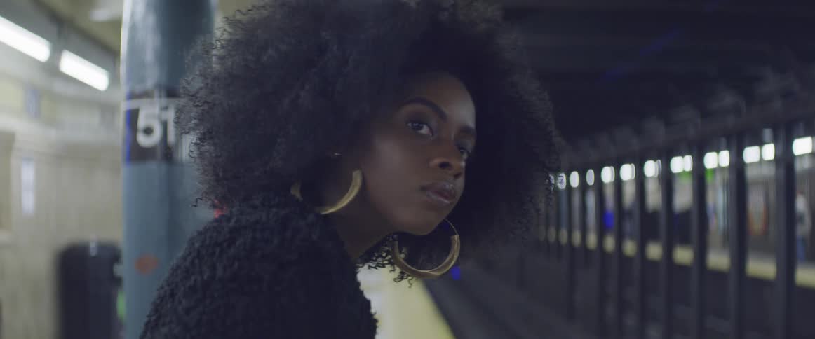 A beautiful woman wearing gold hoop earrings looks down the tunnel while waiting for a train on the subway platform