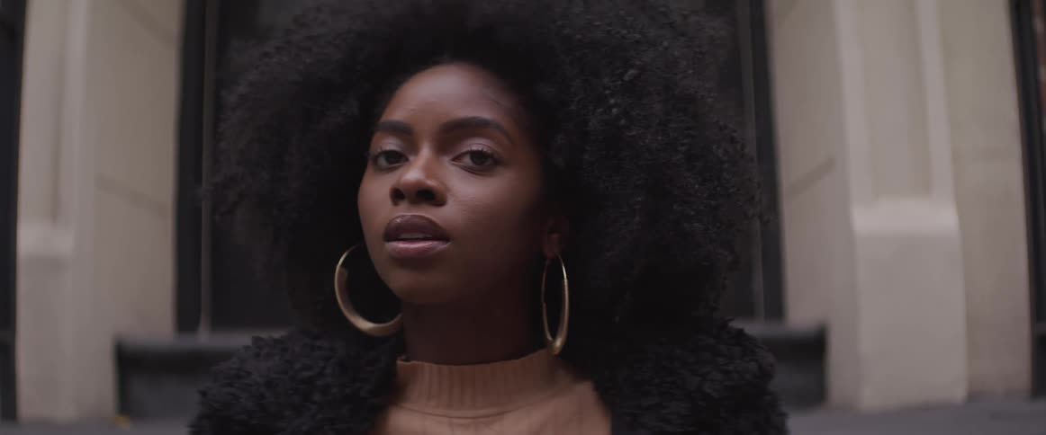 Curly haired black woman sits on the stairs in front of the house