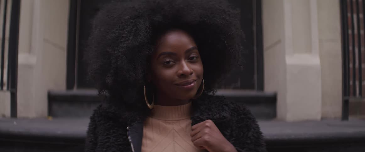 A black woman smiles in front of a buildings doorway