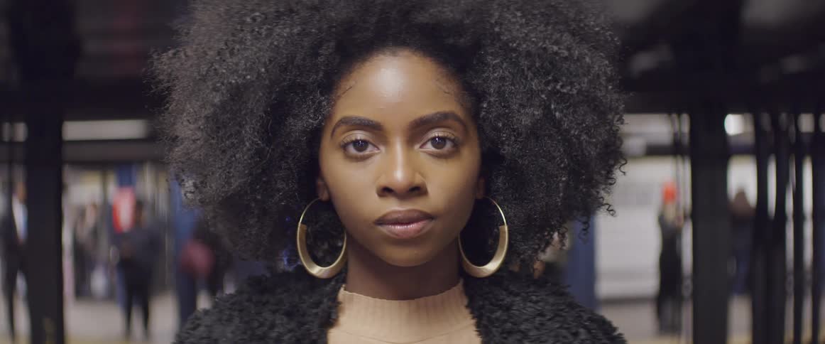 Curly haired black woman stands and stares at the camera