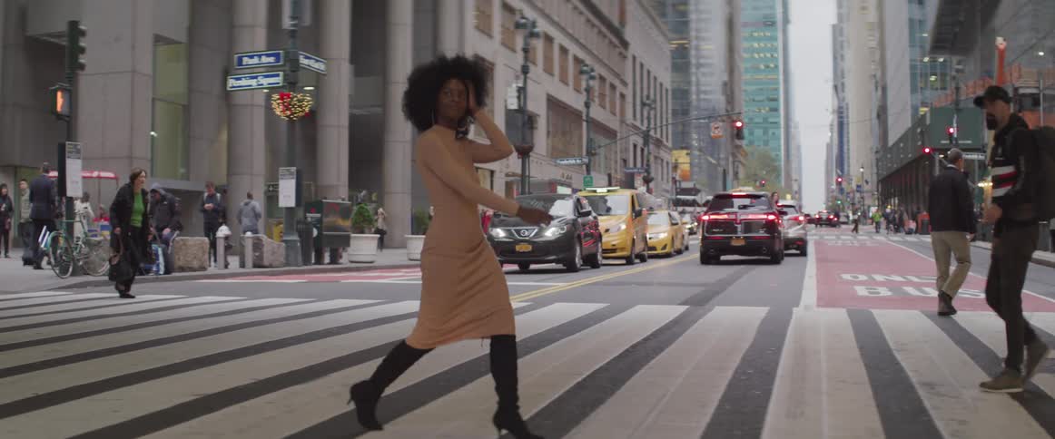 A woman walks a large city crosswalk and another pedestrian notices her