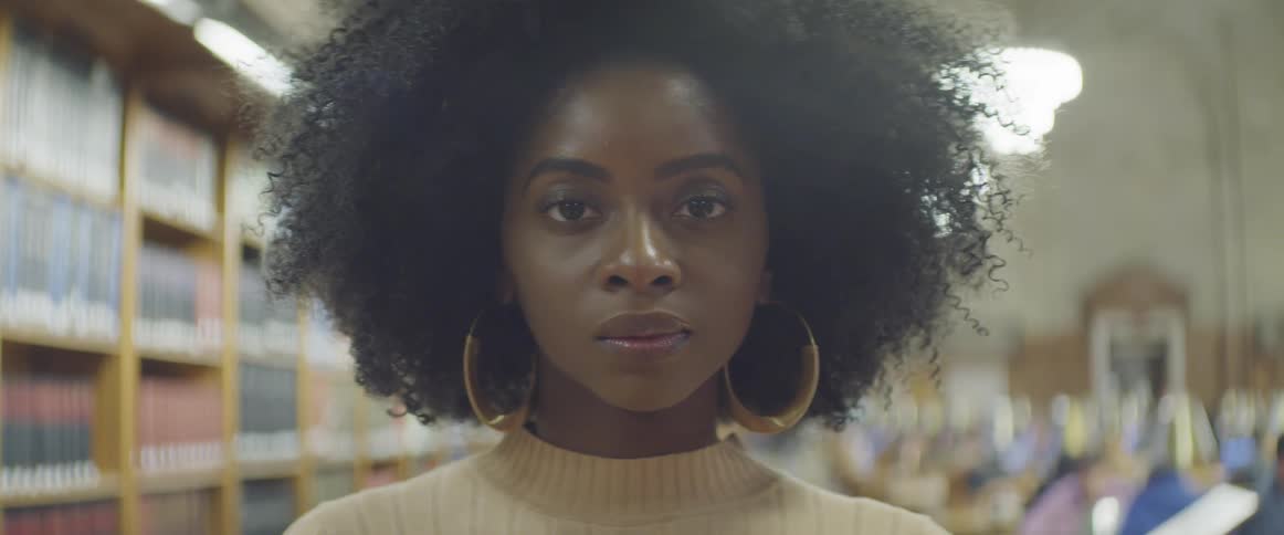 A young black woman looking into the camera while standing in a library