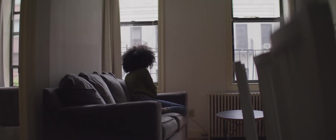 A woman looking out of a window while sitting on a sofa in an apartment