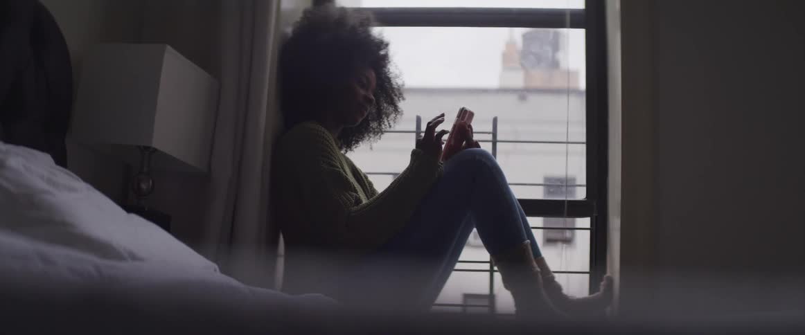 A woman sits with her feet up in a window texting on her phone
