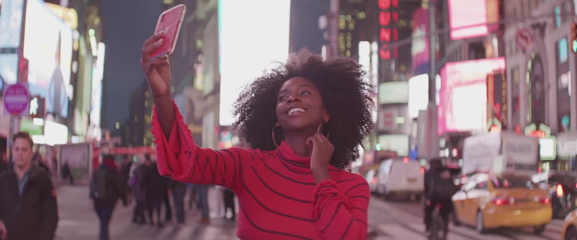 A woman takes selfies on a busy city street