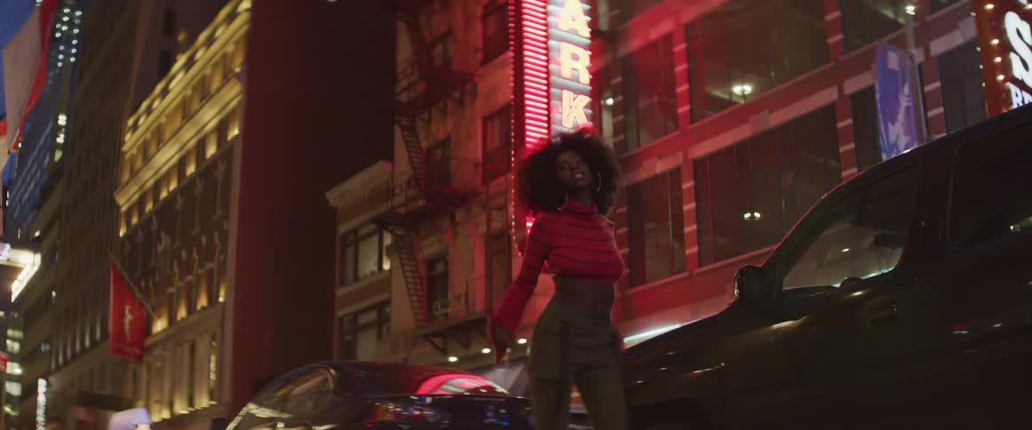 Woman dances on street near cars and neon lit buildings at night