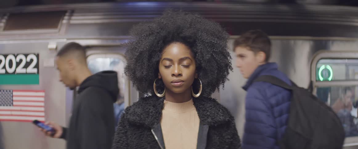 A woman stands with back to the subway trains as people walk past behind her