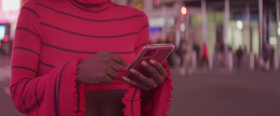 A woman stands outside of a crowded city building scrolling through her cell phone