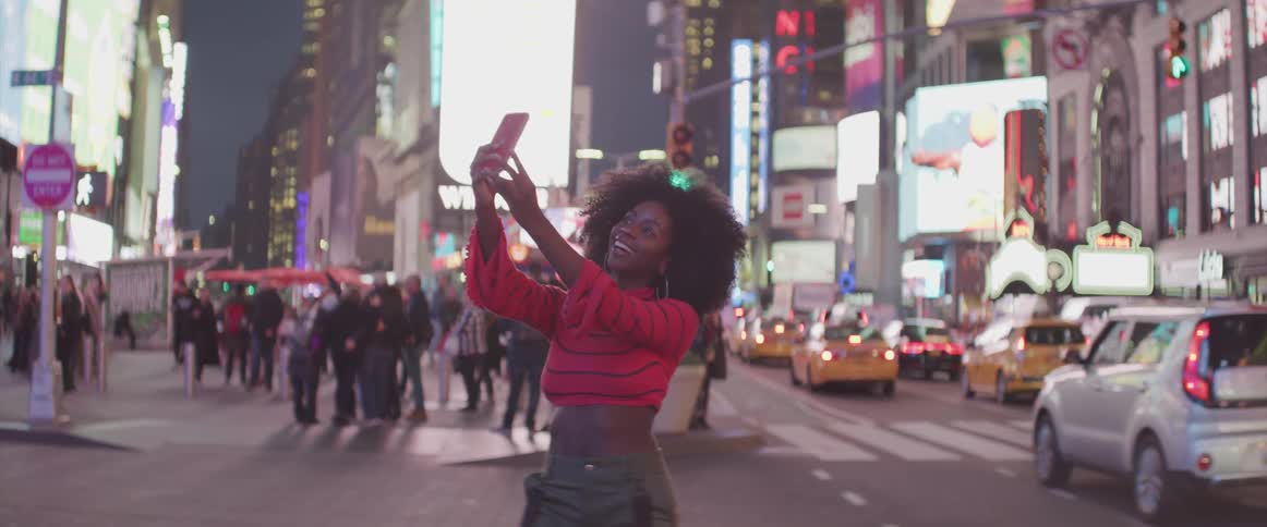 Curly hair black woman takes selfies in the busy street