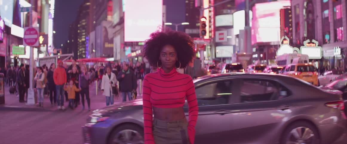 A woman stands on a sidewalk in a large city with traffic behind her