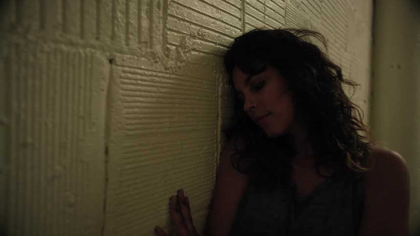A woman leans up against a wall and rubs her hand on it