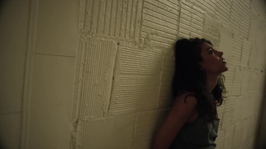 A woman leans against a brick wall