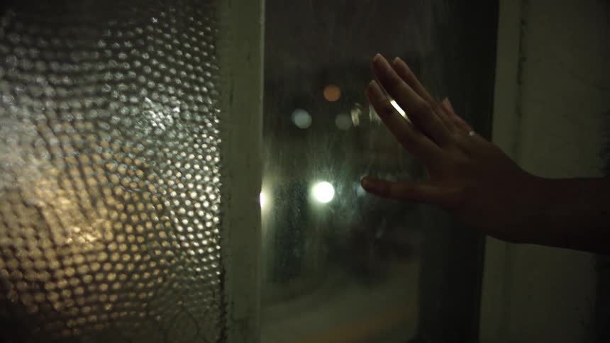 A woman slowly runs her hand down window