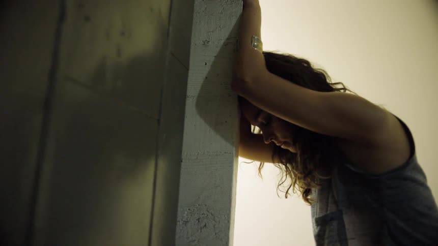 Woman leans her head against a door frame as she slides one hand down the wood
