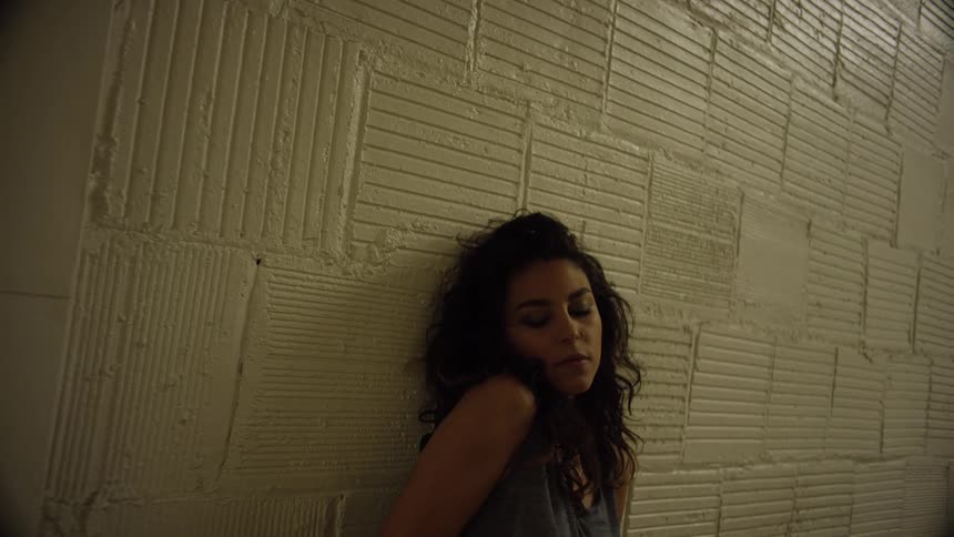A brunette female turns her head by a breeze block wall