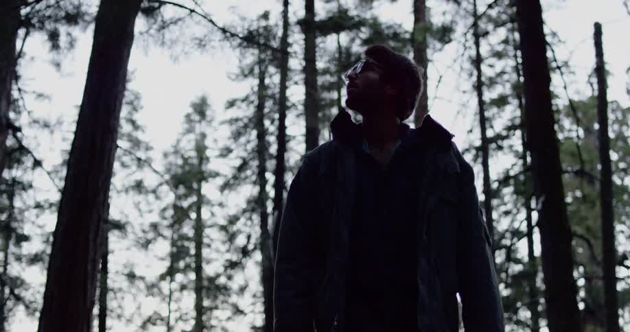 Man in winter jacket walking in forest then stopping to look around