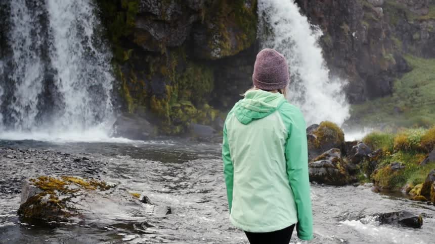 A woman is standing on the side of a large waterfall looking over
