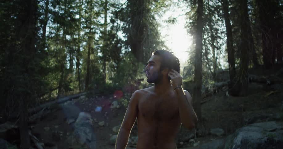 Shirtless man shaking wet hair from swimming in the forest